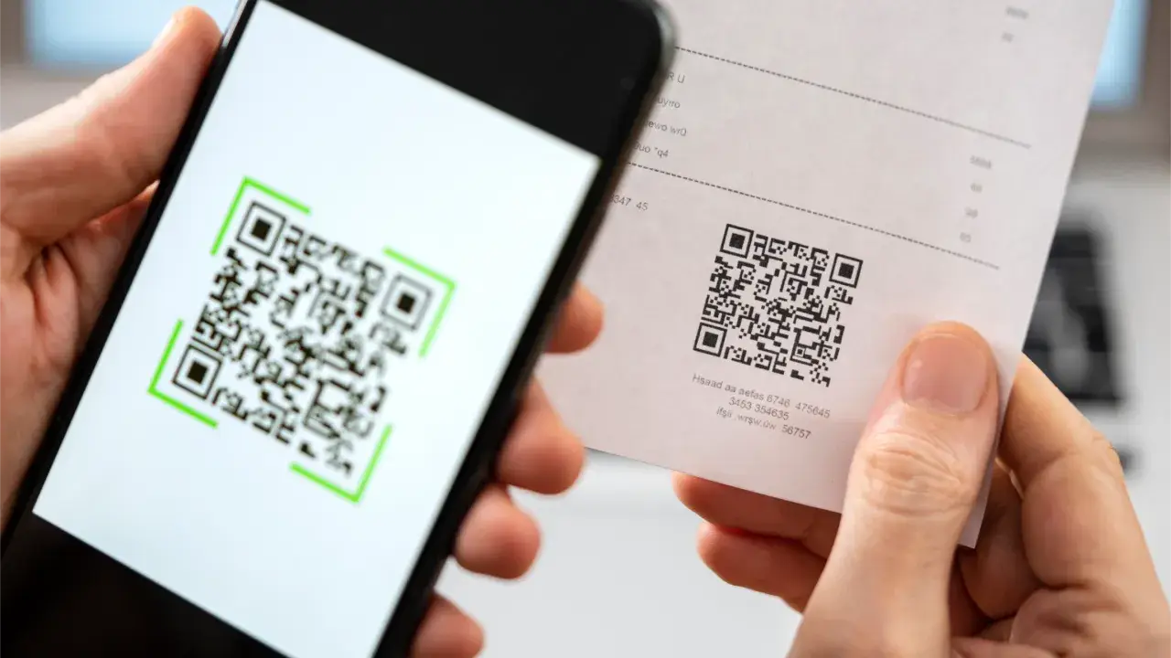 Nahaufnahme einer Person, die einen Papierbeleg mit einem QR-Code in der Hand hält und den Code mit einem Smartphone scannt